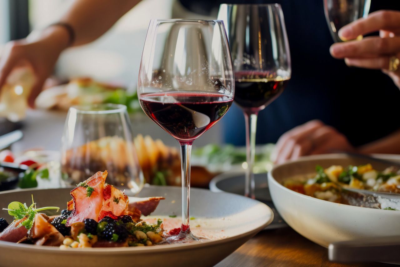Um grupo de pessoas está sentado à mesa comendo e bebendo vinho.