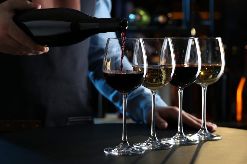 Um barman está servindo vinho em uma fileira de taças de vinho.