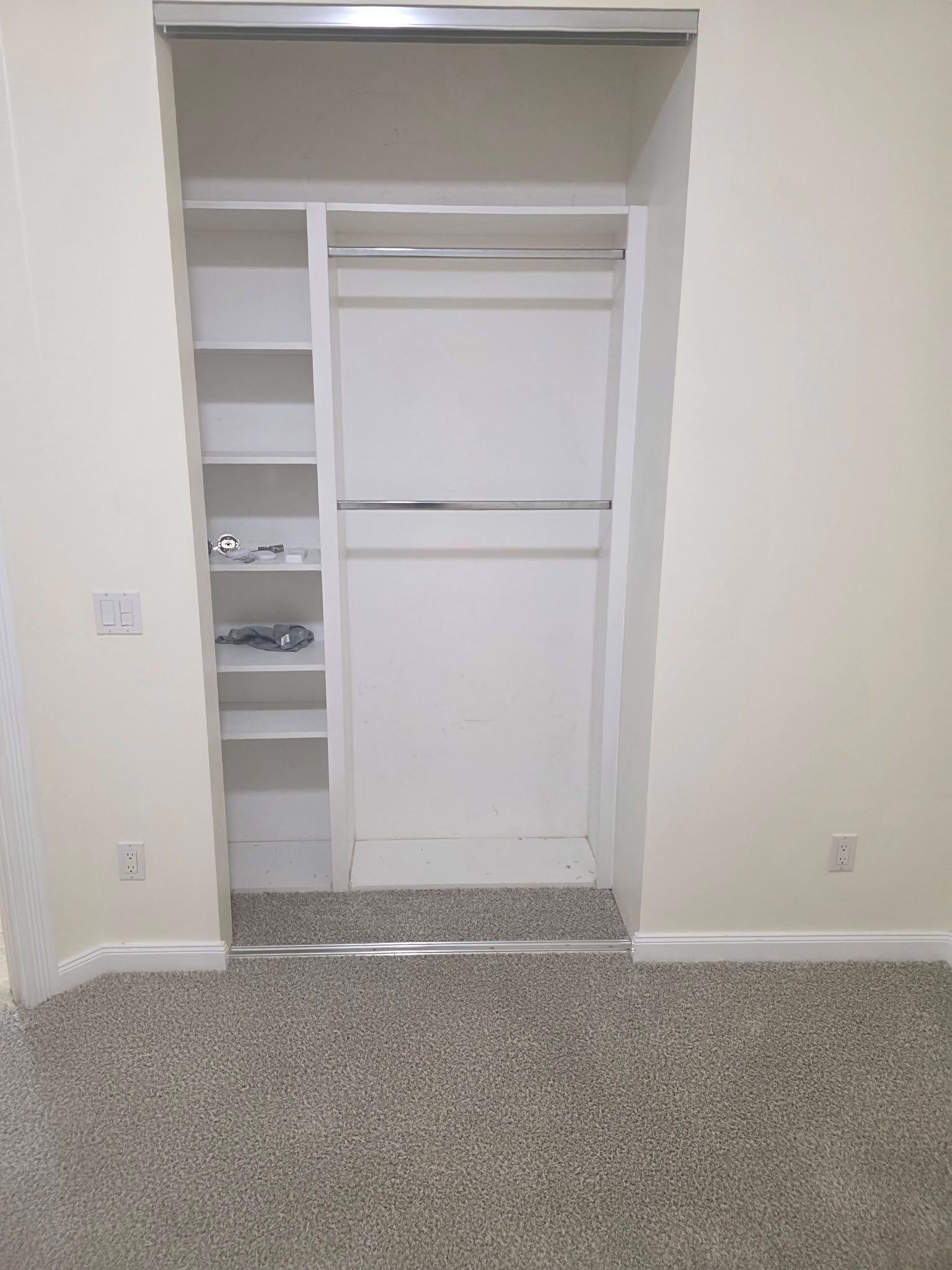 Empty white closet with shelves and a hanging rod, viewed from a carpeted room.