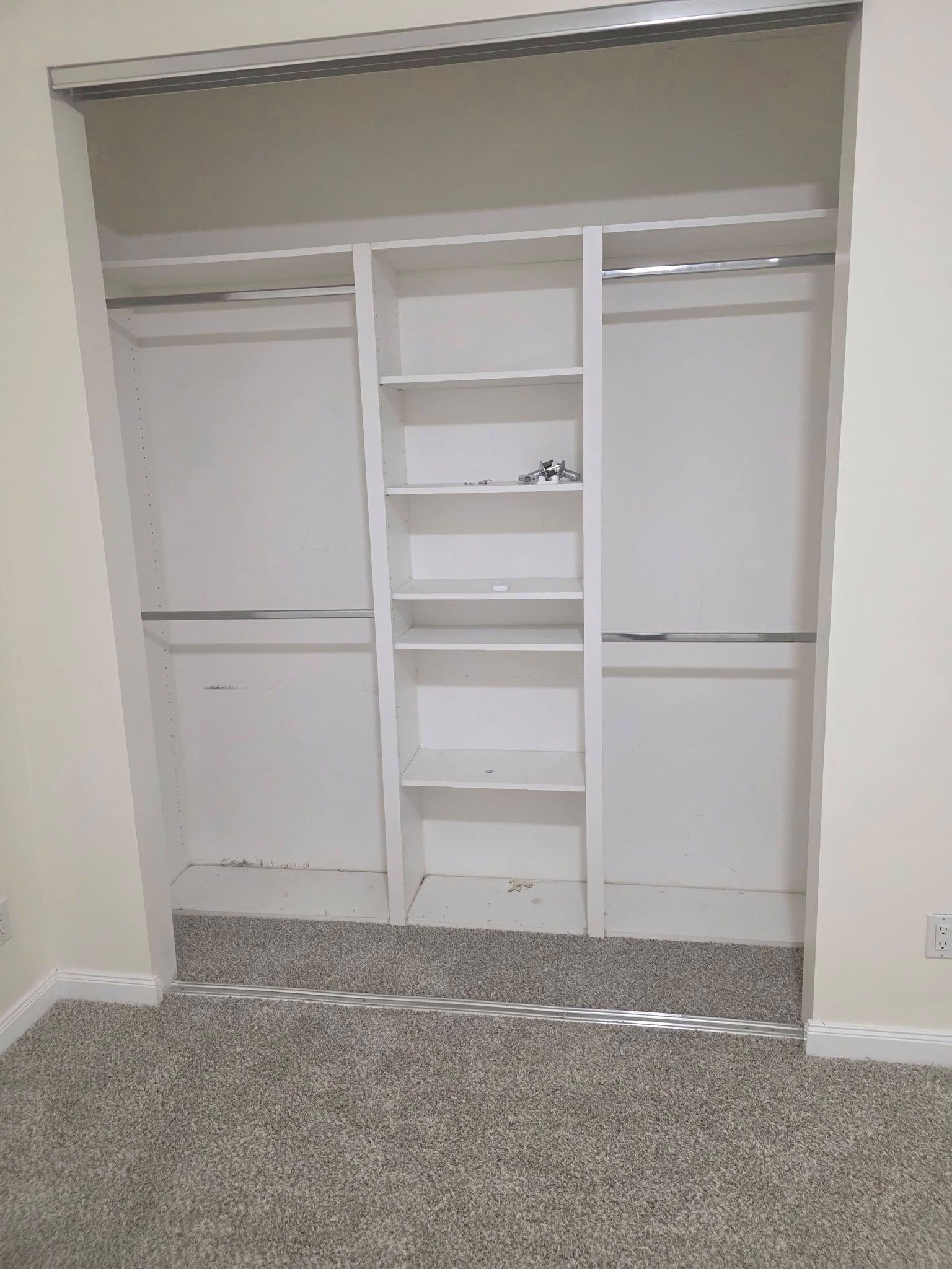 Empty closet with white shelving, hanging rods, and carpeted floor.