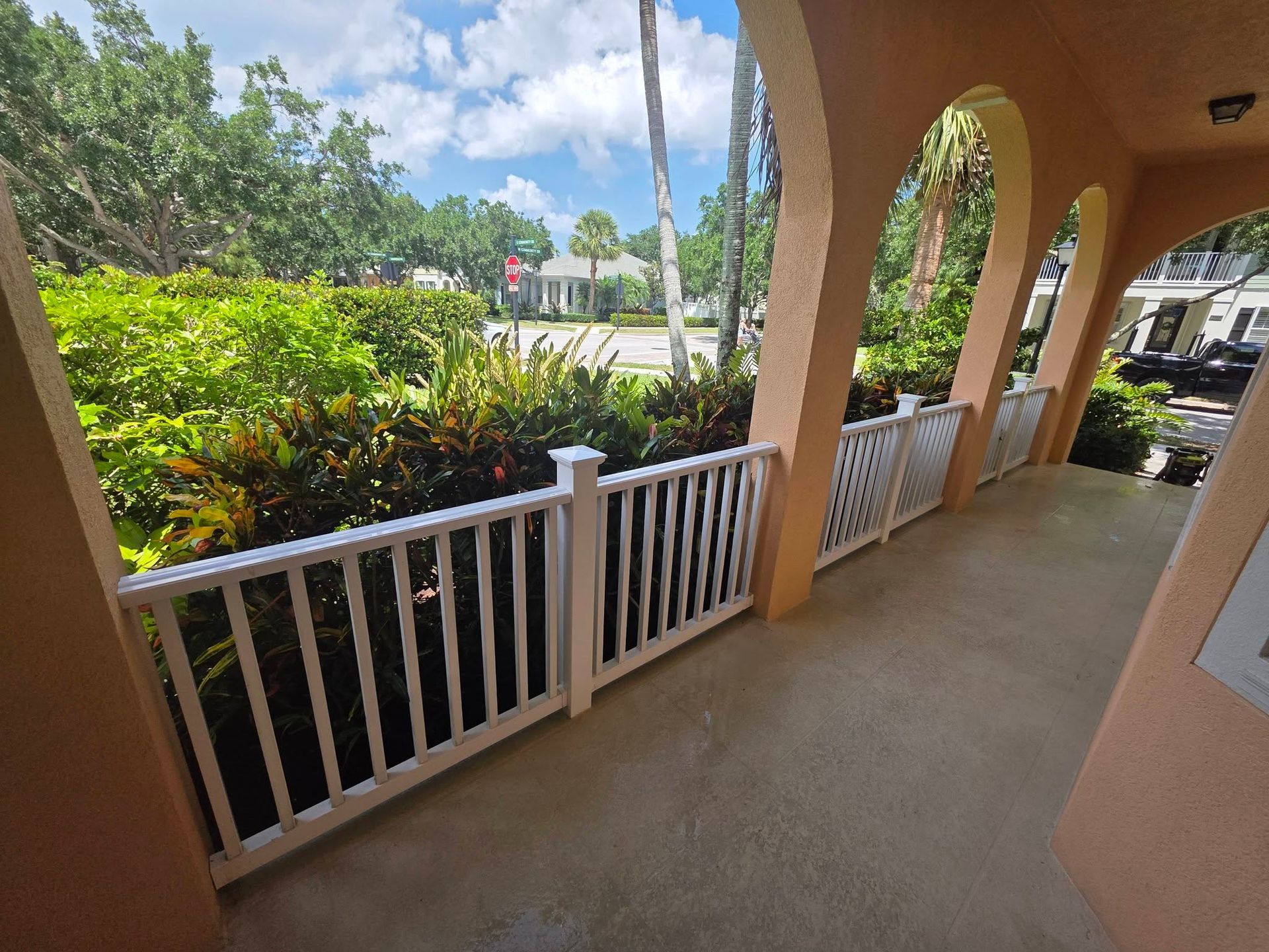 Covered porch with white railing, arches, and tropical landscaping outside