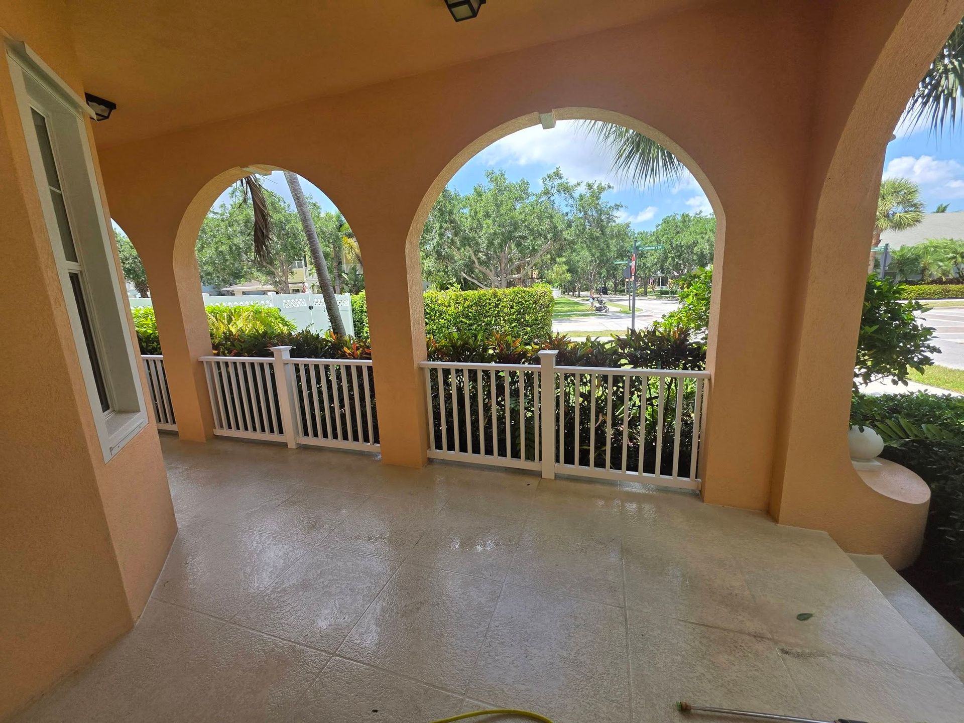 Covered porch with peach arches, white railing, and a view of green trees and a road beyond.