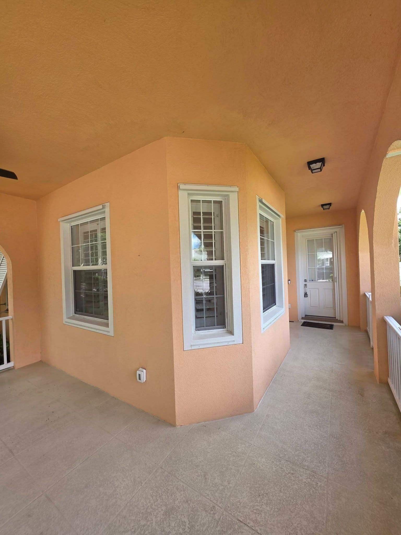 Covered patio with peach stucco walls, white-trim windows, and carpeted floor leading to a doorway