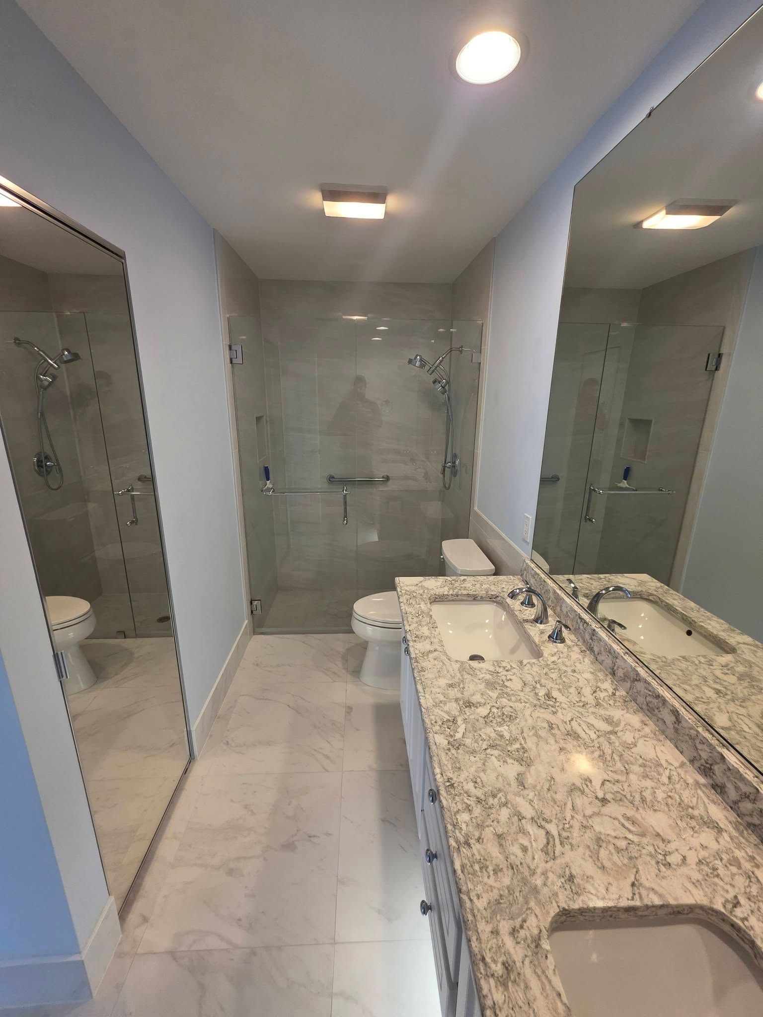 Modern bathroom with double vanity, large mirror, glass shower, and granite countertops.
