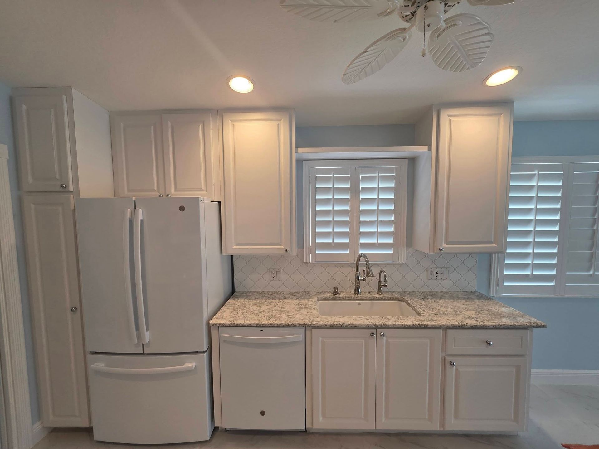 Bright white kitchen with cabinets, granite countertops, refrigerator, and plantation shutters