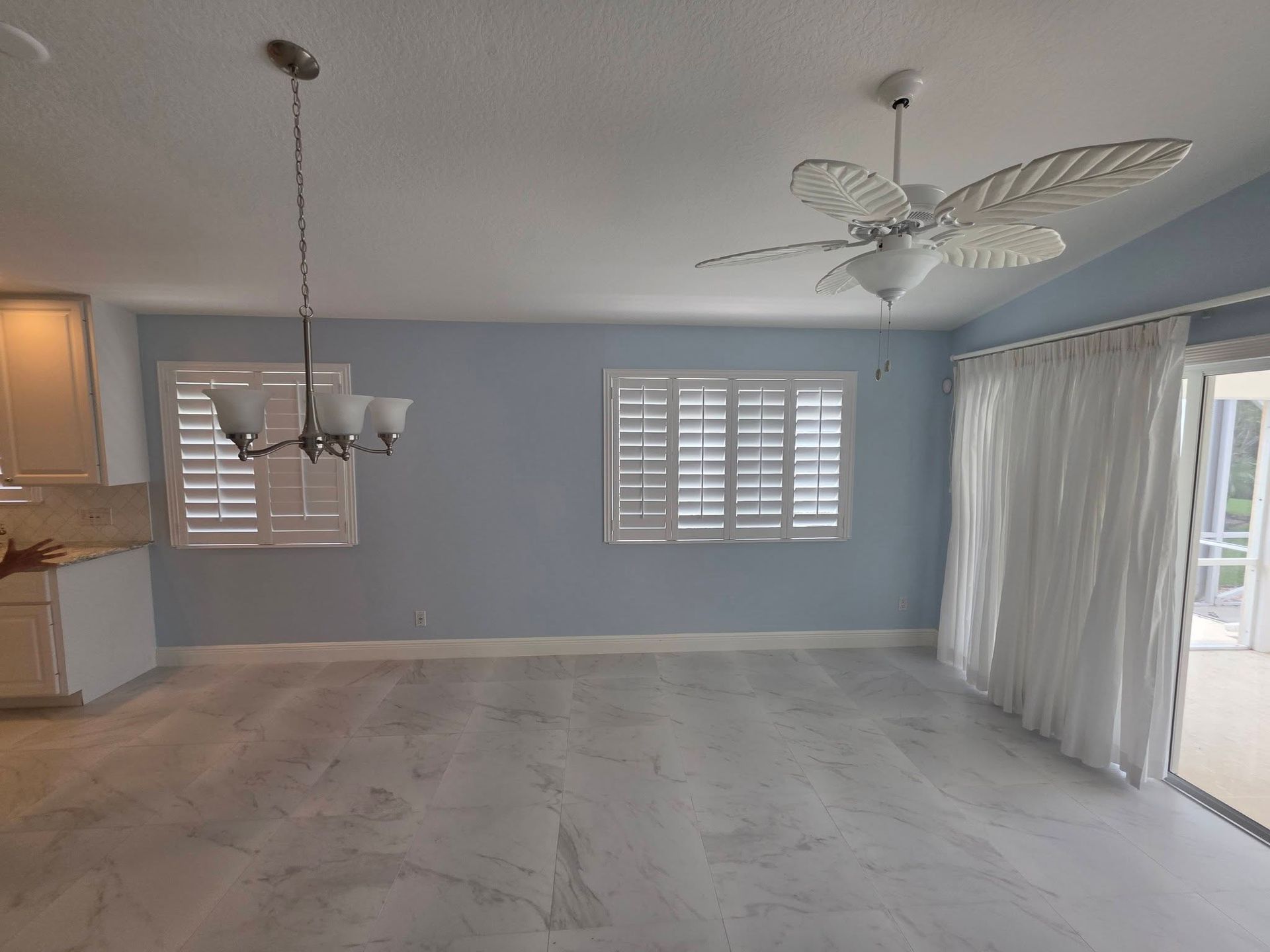 Empty gray dining room with tile floor, chandelier, ceiling fan, and sliding glass doors with curtains