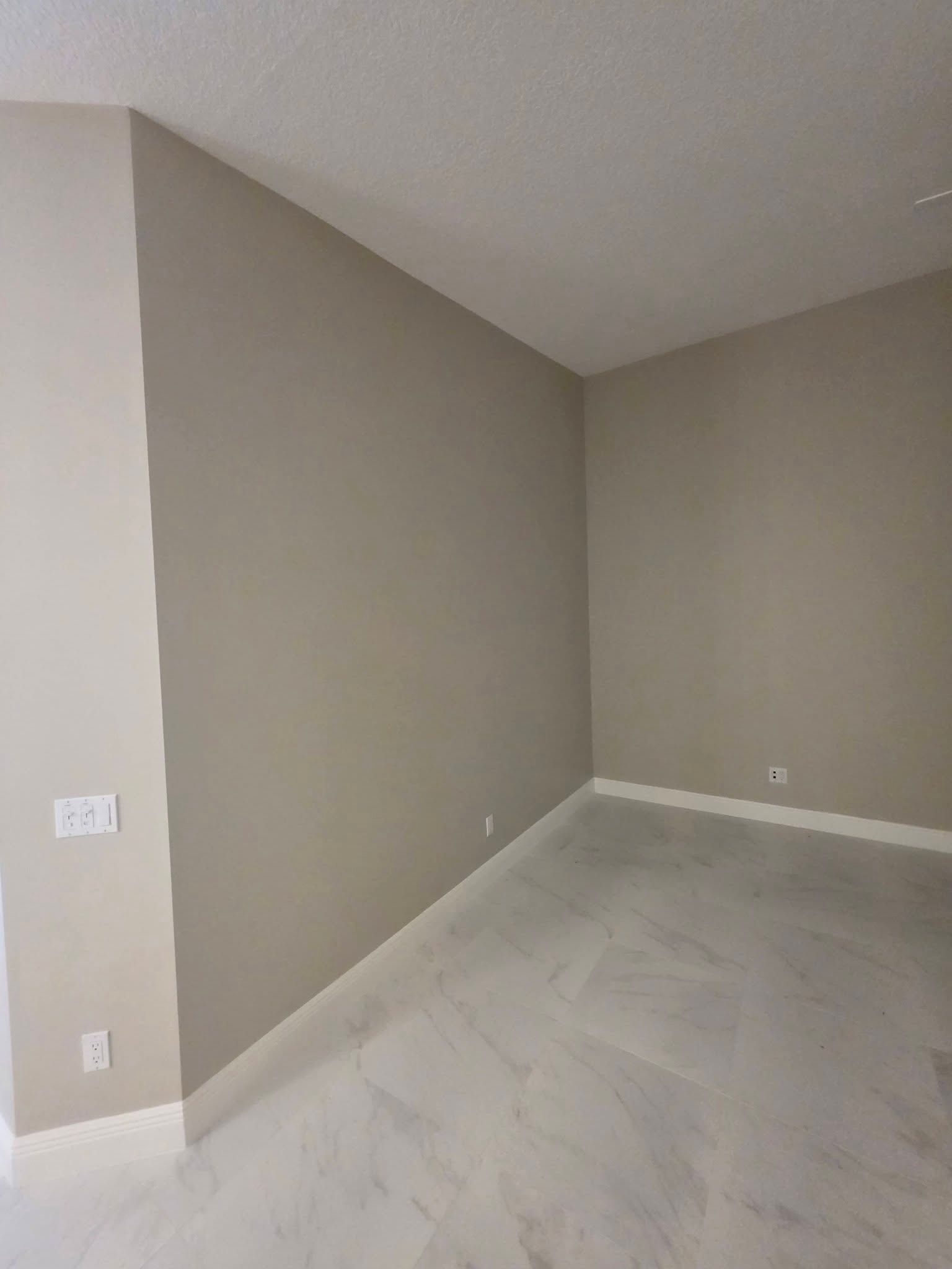 Empty beige room with gray carpet and white baseboards, viewed from a corner