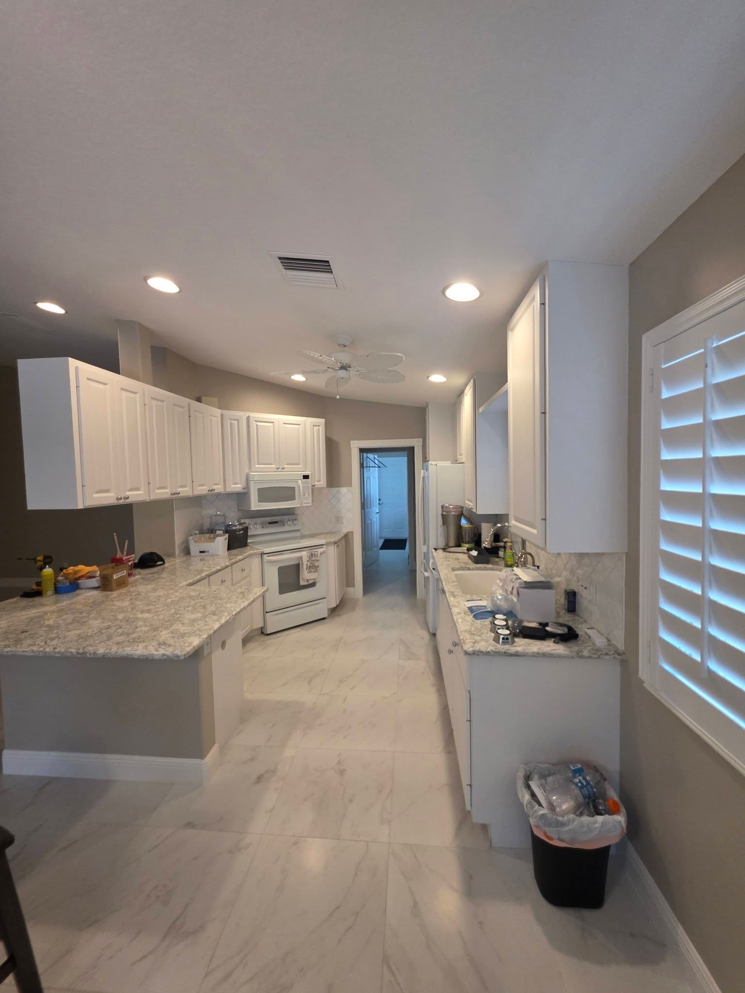 Bright modern kitchen with white cabinets, granite island, and light wood floors, viewed from the entry.