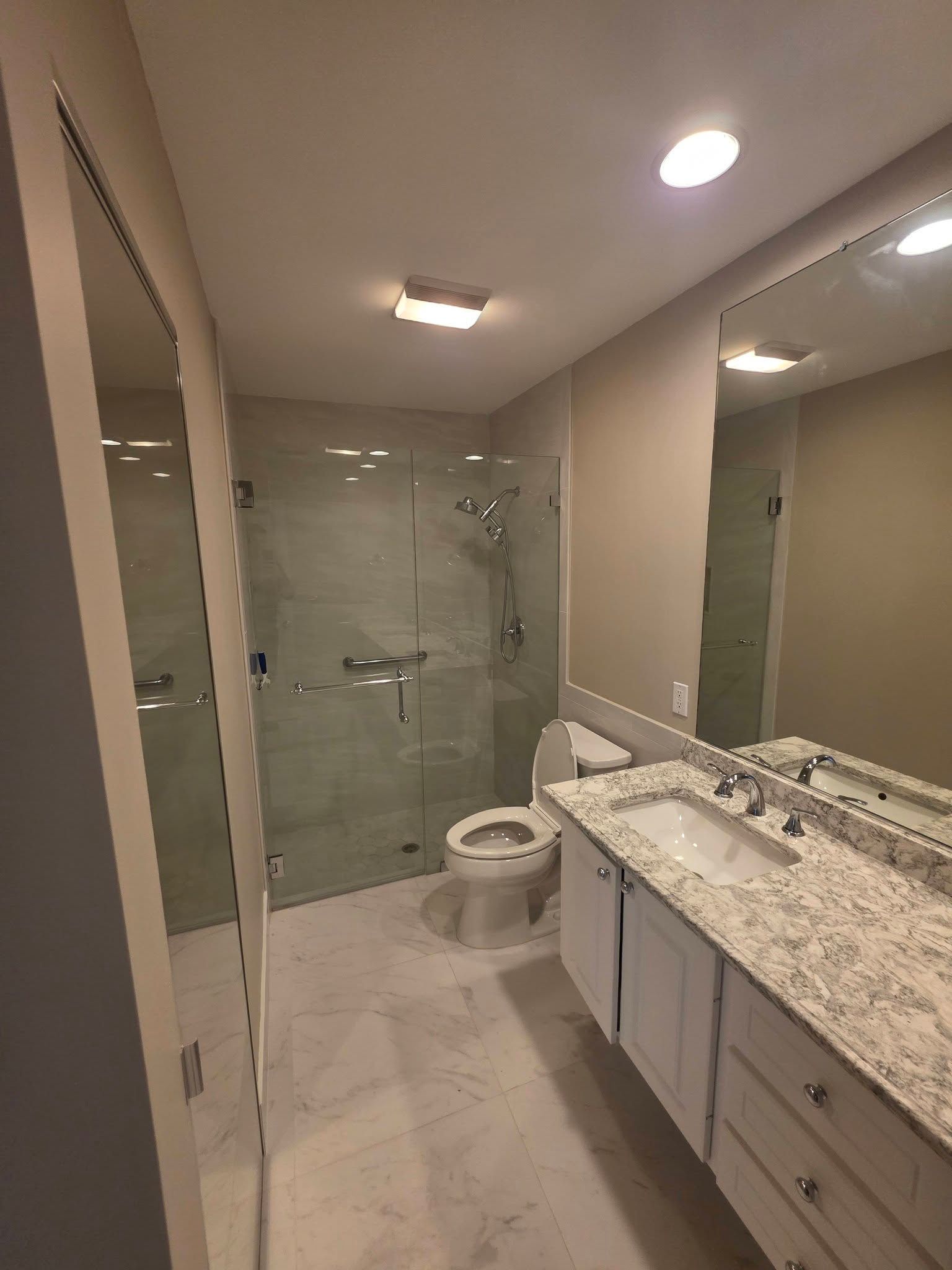 Modern bathroom with double vanity, large mirror, toilet, and glass shower doors.