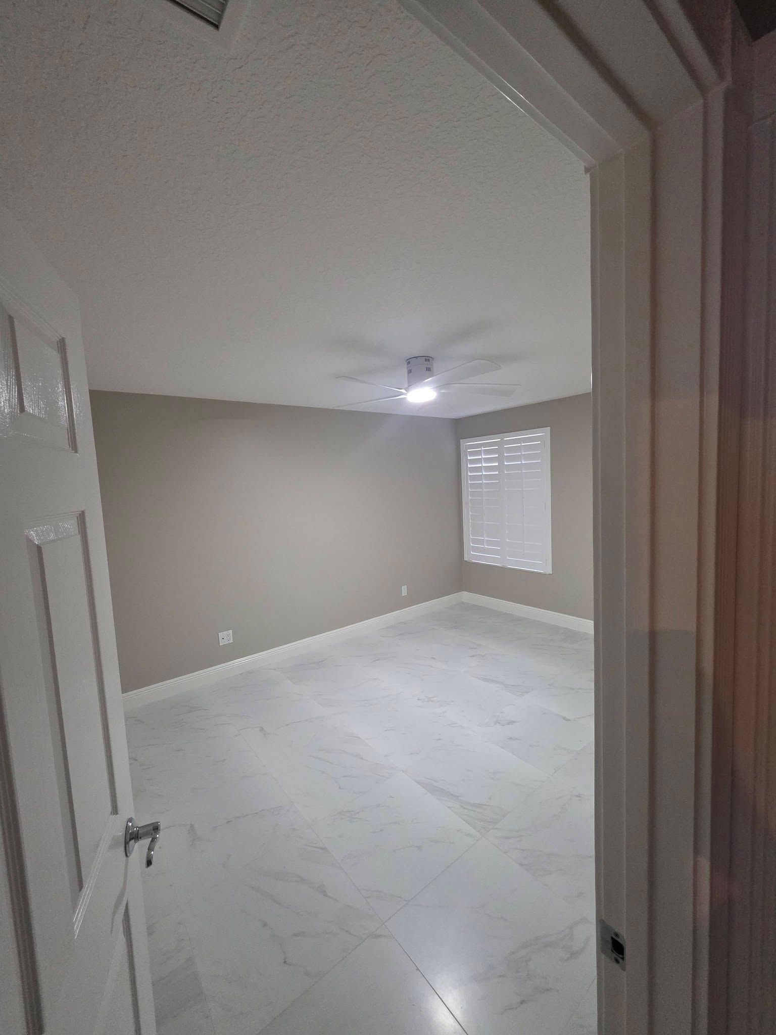 Empty beige bedroom with white carpet, ceiling fan, and window with blinds