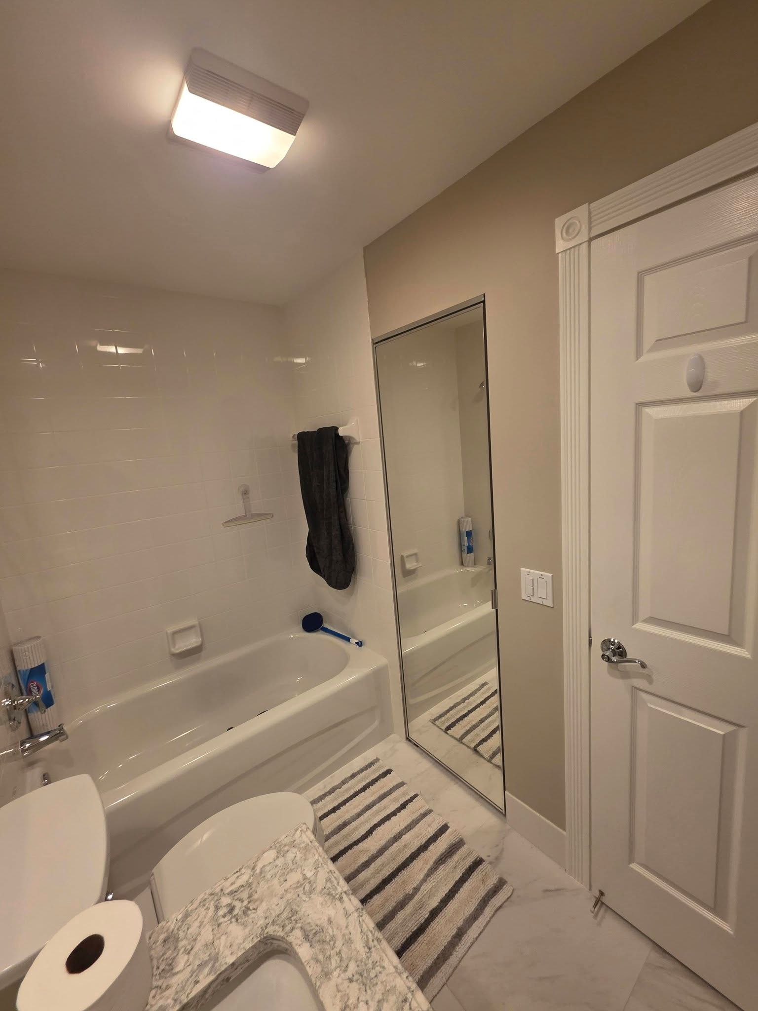 Bright bathroom with bathtub, striped rug, and mirrored closet door near a white door.