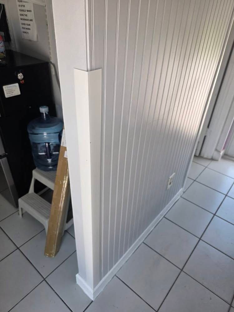 Narrow hallway with white beadboard walls, tiled floor, and a water cooler on a step stool by a doorway
