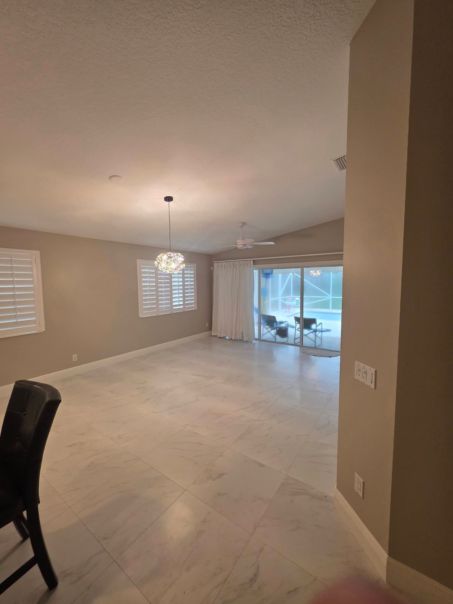 Empty beige living-dining room with tile floor, windows, and sliding glass doors to a patio