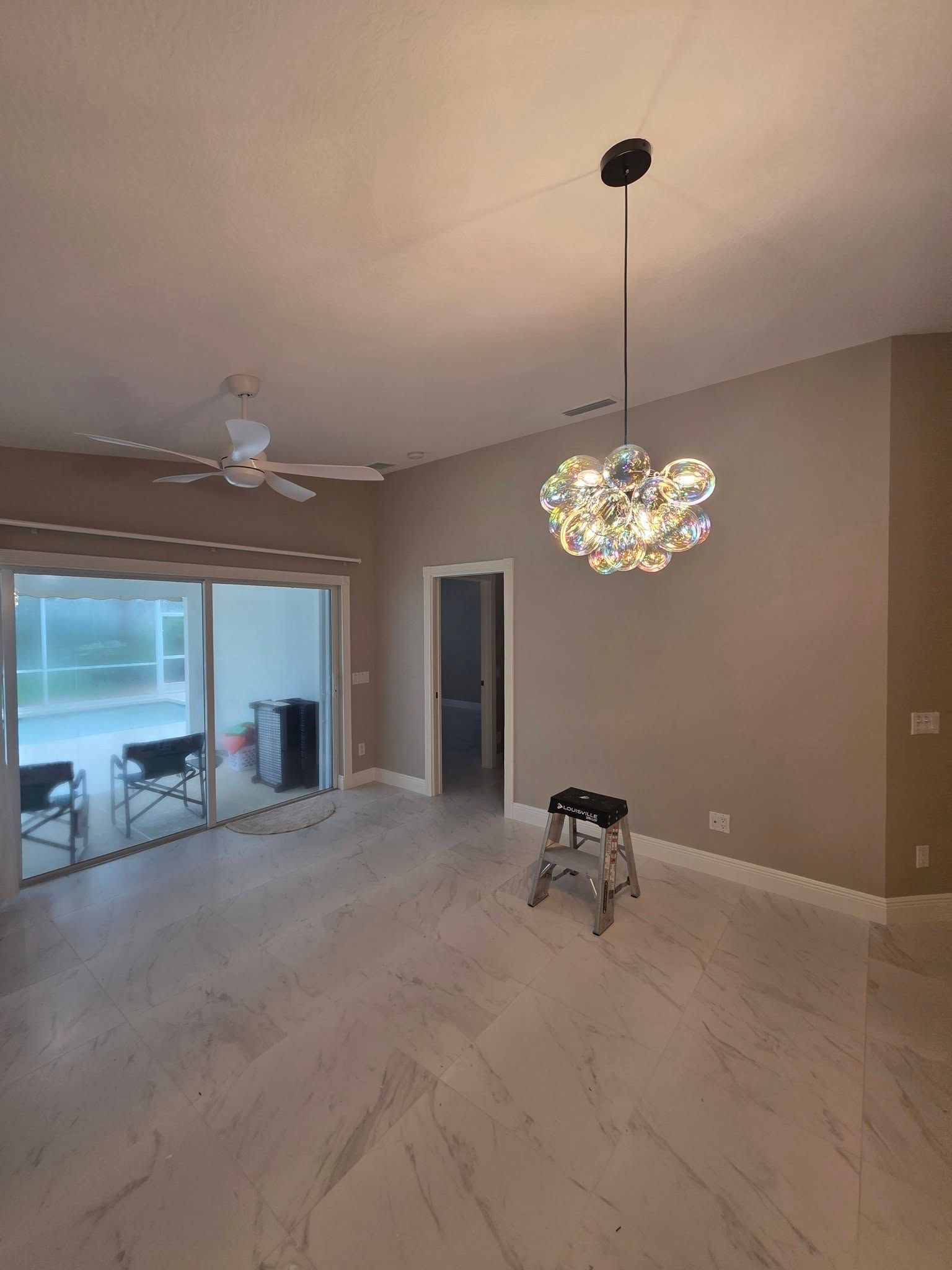 Empty modern living room with marble floor, ceiling fan, and a colorful pendant light over sliding glass doors.
