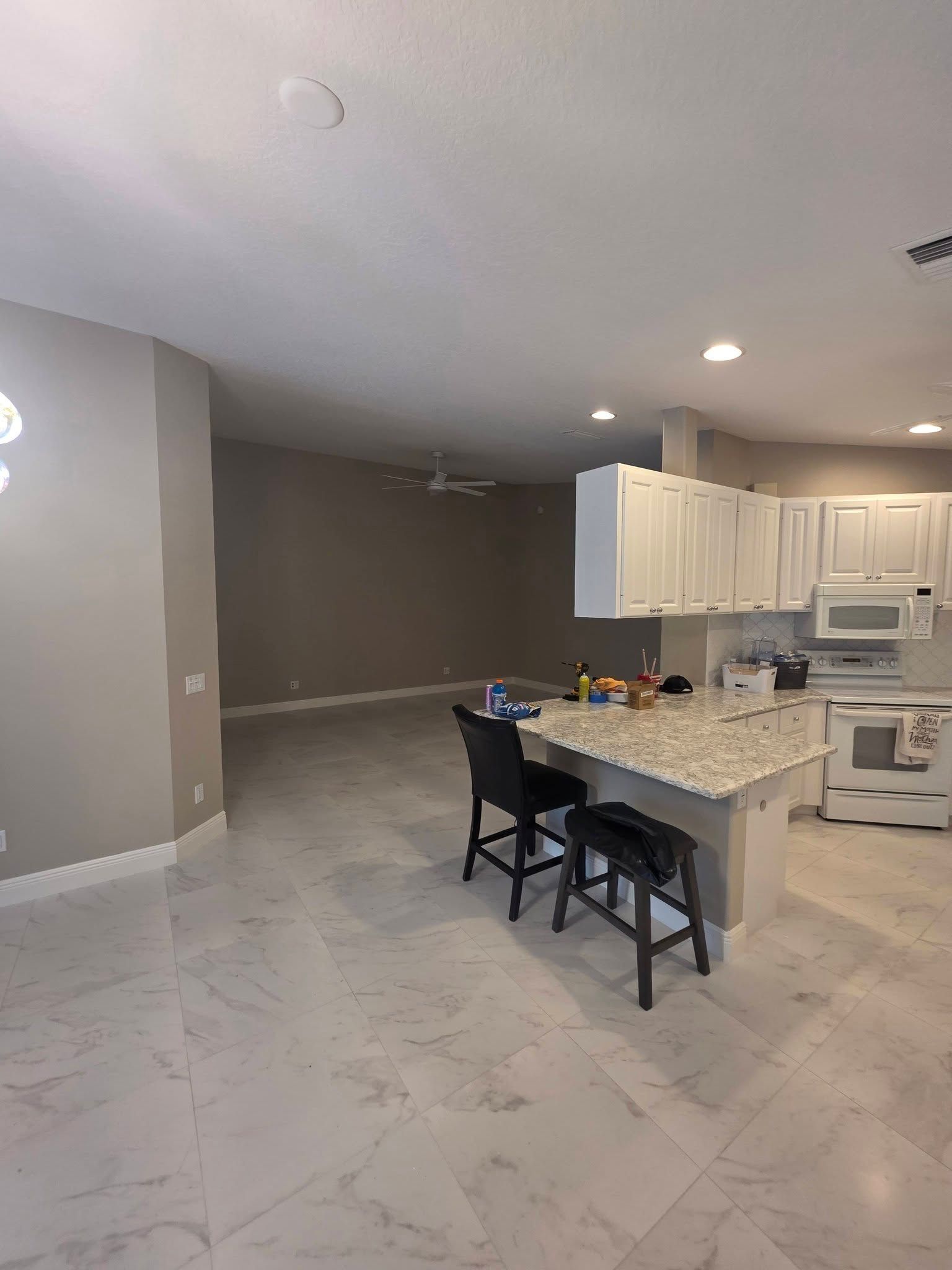 Open kitchen and dining area with white cabinets, marble floor, and a granite island with chairs.