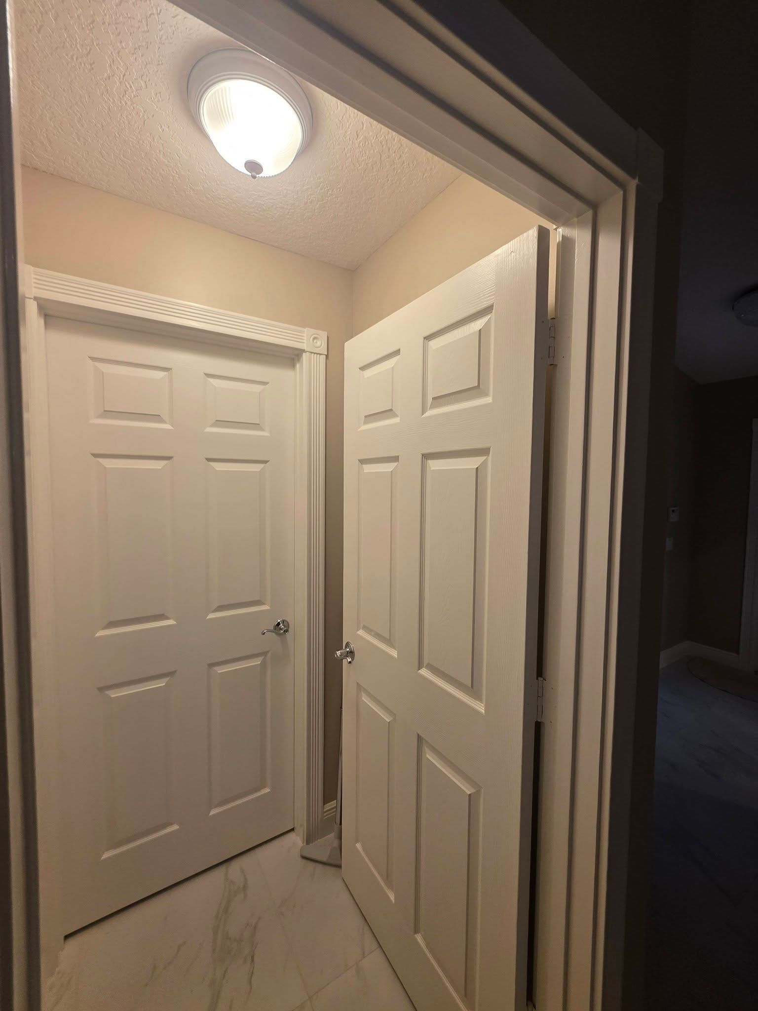 Open white closet doors in a beige hallway under a ceiling light.