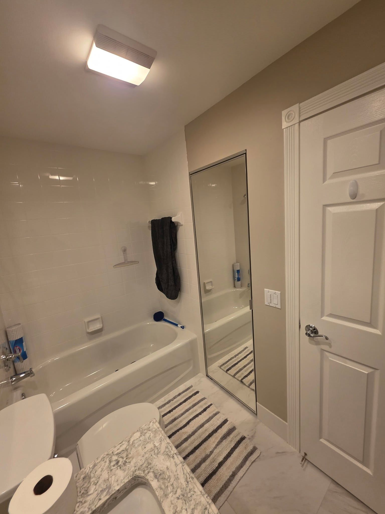 Bathroom with white tub, mirror, striped rug, and towel hanging on the wall.