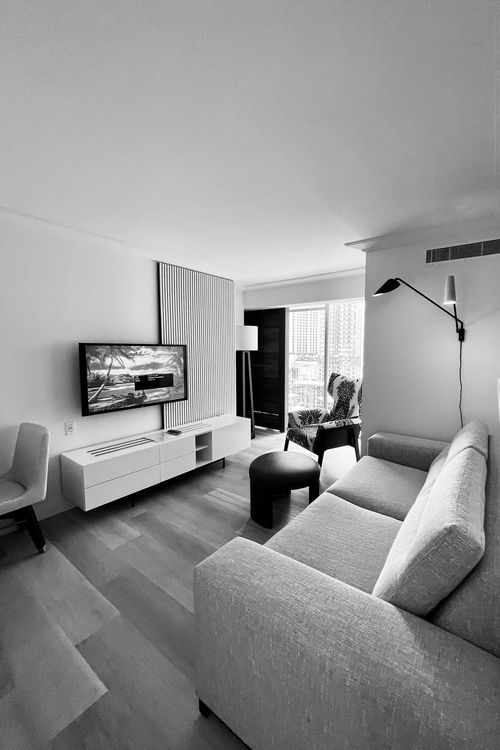 Modern living room with gray sofa, TV, floor lamp, and balcony doors.