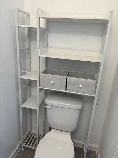 White toilet with over-toilet shelving and two drawers in a narrow bathroom storage unit