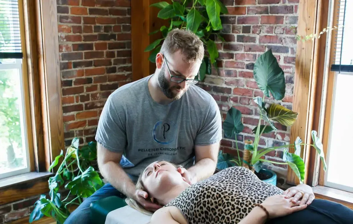 Chiropractor working on a client in a bright brick-walled room with plants and large windows