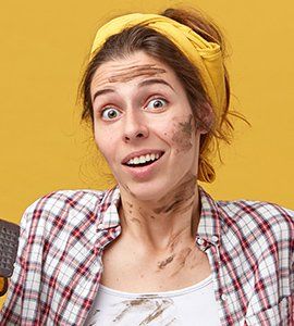 Woman with dirt on face and shirt, wearing yellow headband, surprised expression, against yellow background.