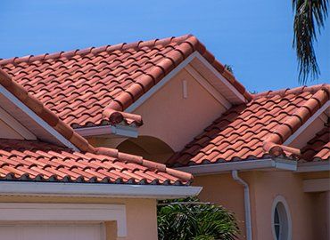 Red tile roof on a pale peach house against a clear blue sky.