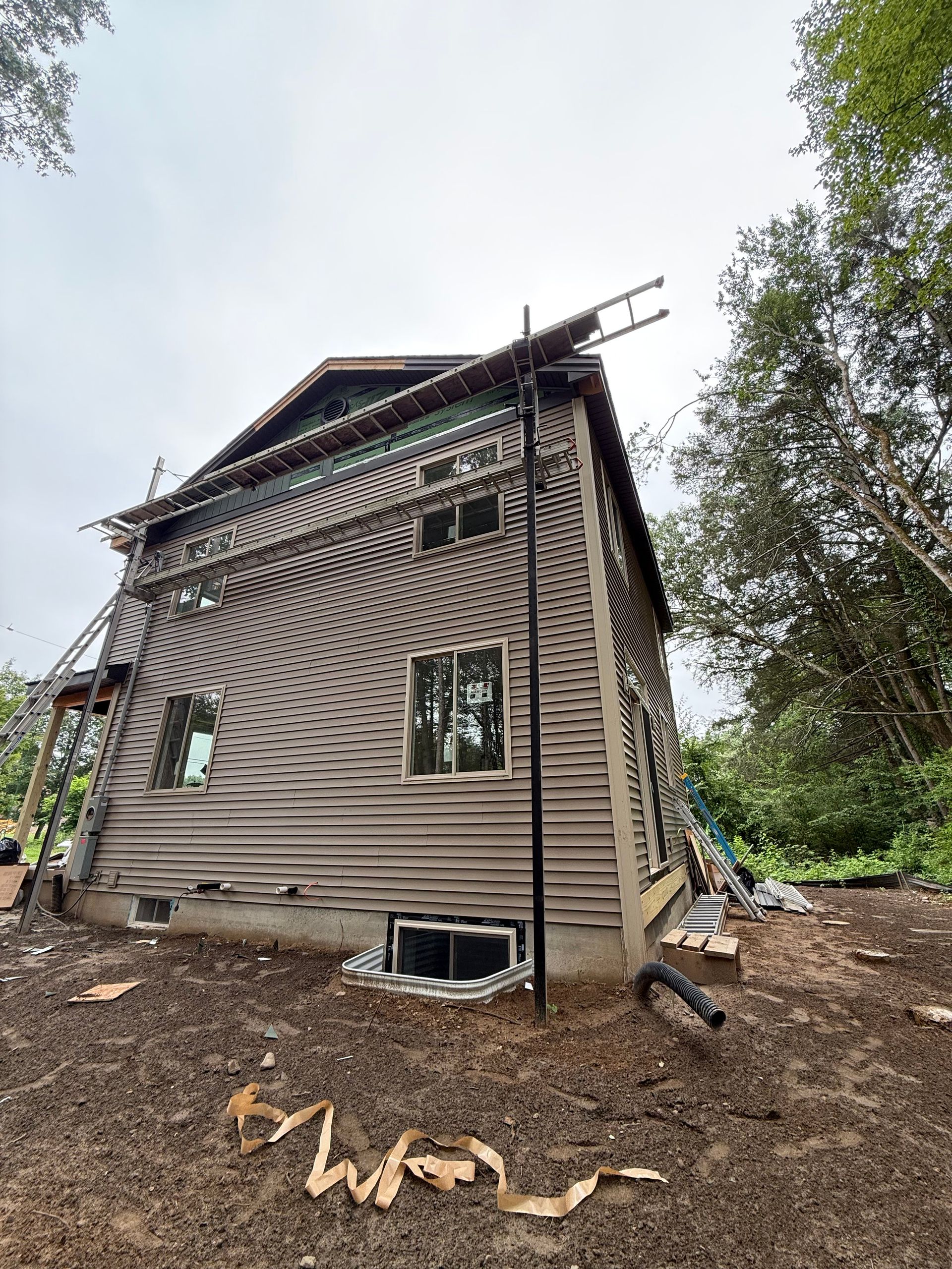 Wooden house under construction with scaffolding, windows, and surrounding greenery.