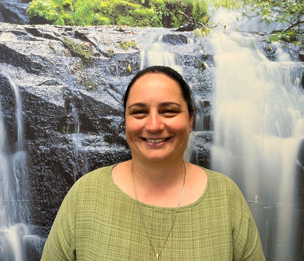Woman smiling, wearing a green top, in front of a waterfall background.— Axis Chiropractic In Cairns City, QLD