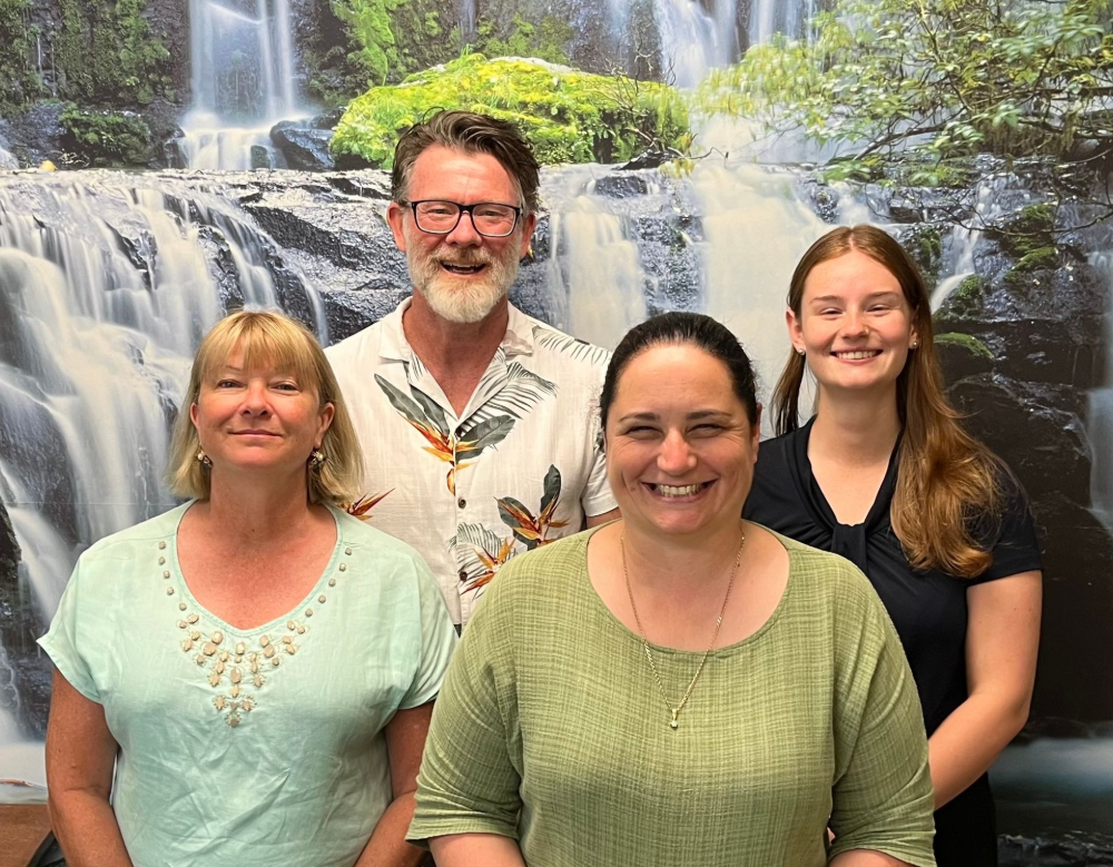 Four people smiling in front of a waterfall backdrop— Axis Chiropractic In Cairns City, QLD