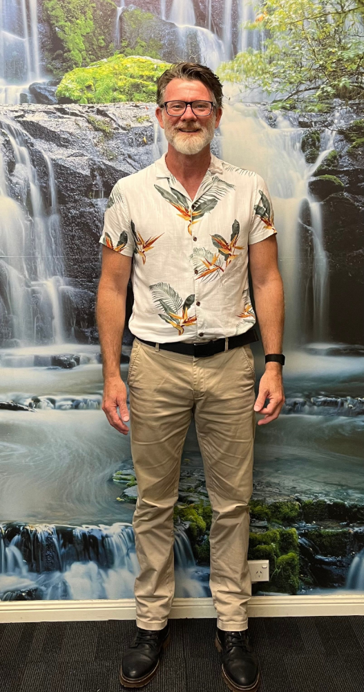 Man in floral shirt and khaki pants stands in front of a waterfall backdrop— Axis Chiropractic In Cairns City, QLD