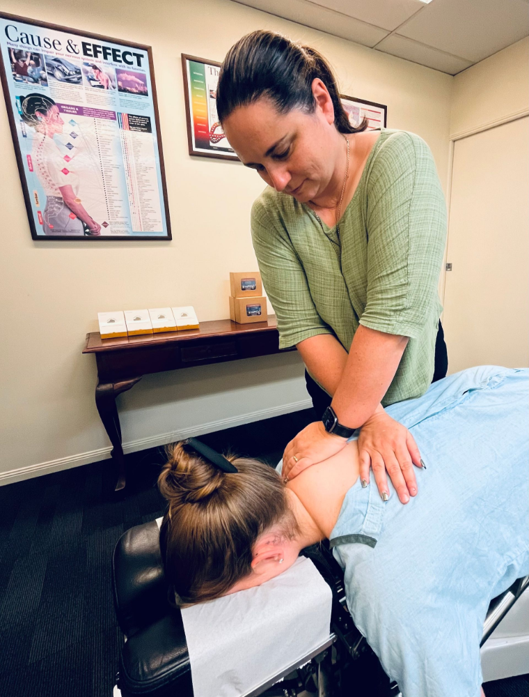 Chiropractor adjusting patient's neck in an office. A woman in a green shirt leans over a patient on a table.— Axis Chiropractic In Cairns City, QLD