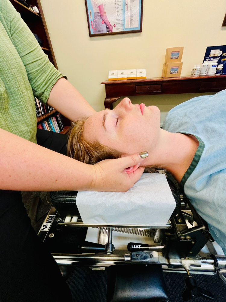 Person receiving chiropractic neck adjustment. Hands on head and neck, eyes closed, clinic setting— Axis Chiropractic In Cairns City, QLD