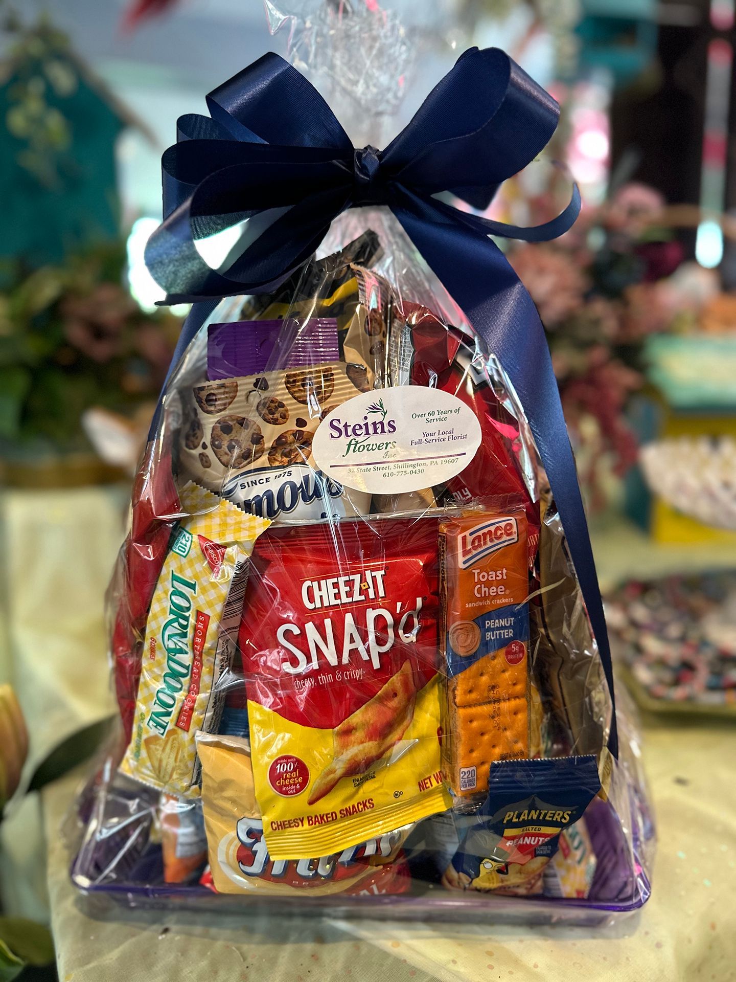 A basket filled with snacks and a blue bow is sitting on a table.