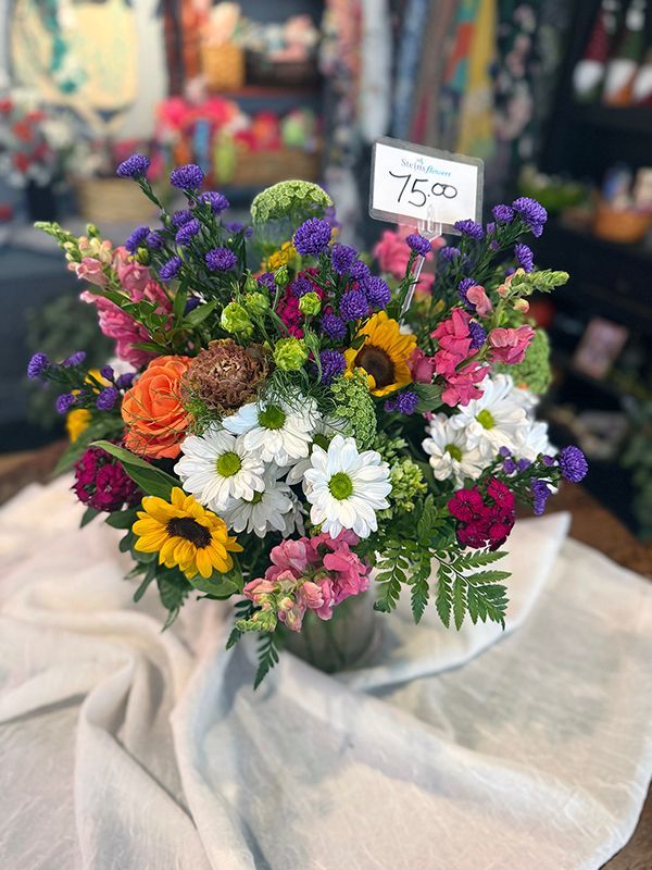 Colorful mixed flower bouquet with daisies, roses, and purple blooms in a wrapped vase at a market stall
