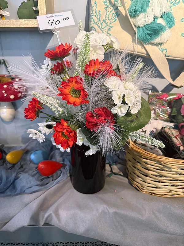 Artificial flower bouquet with red, white, and silver blooms in a black vase on a table