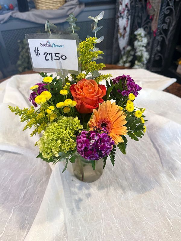 Mixed flower bouquet in a glass vase with a $15 sign on a table in a shop
