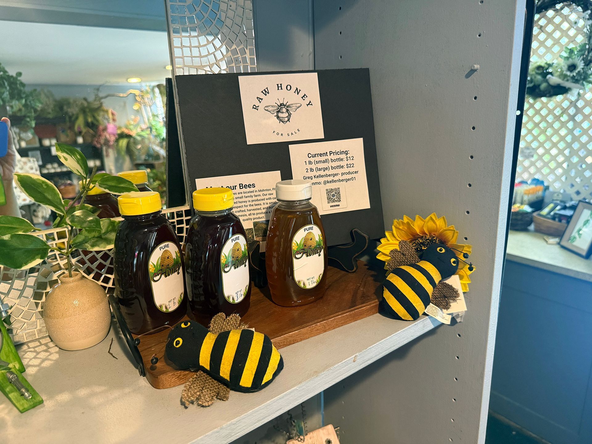 Honey jars and bee-themed gift display on a shelf with sunflowers and small signs