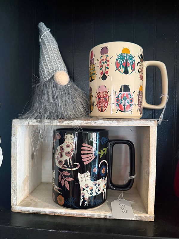 Two decorated mugs and a gnome figurine displayed on a small white shelf