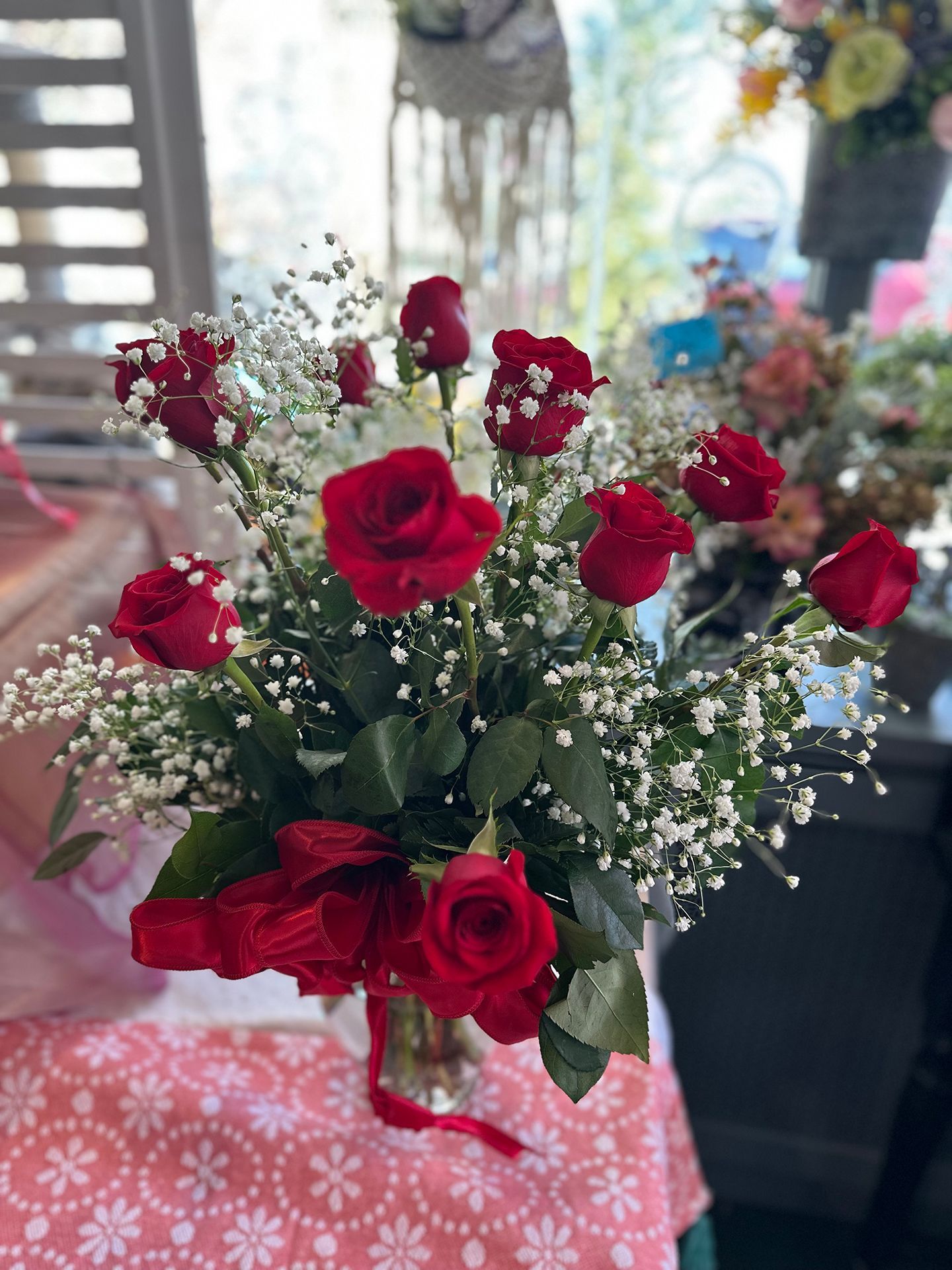 A vase filled with red roses and baby 's breath is sitting on a table.