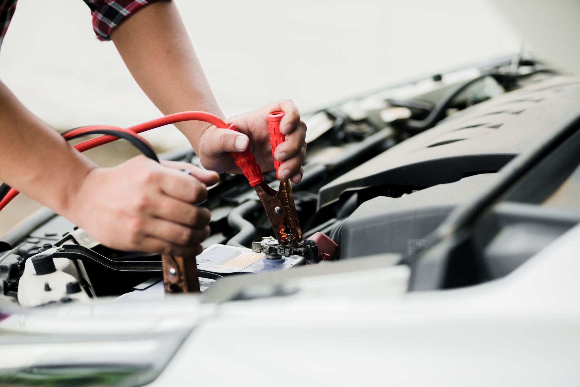 A person attaches red and black jumper cables to a car battery to jump-start an engine.