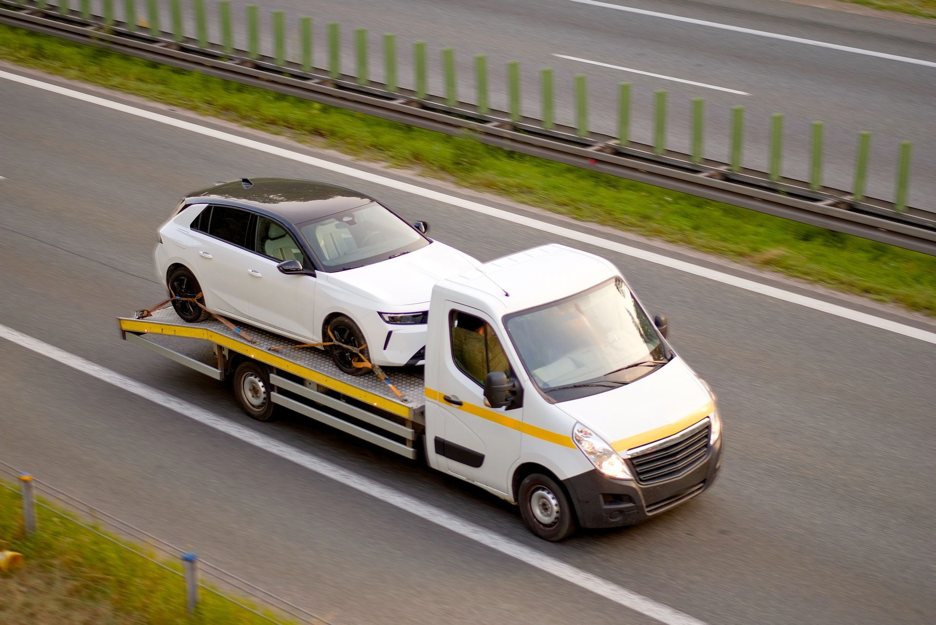 A white car with a black roof being transported on a flatbed tow truck on a highway.