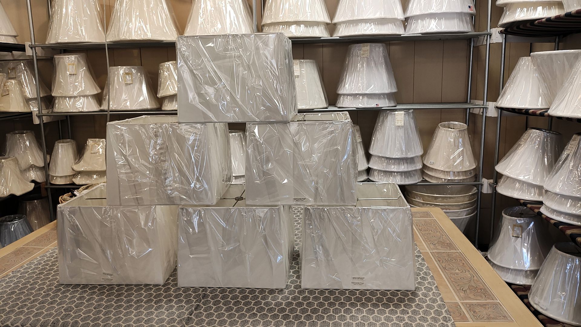 Stacked silver-gray lampshades on a display table, with shelves of similar shades in the background. Avon, CT