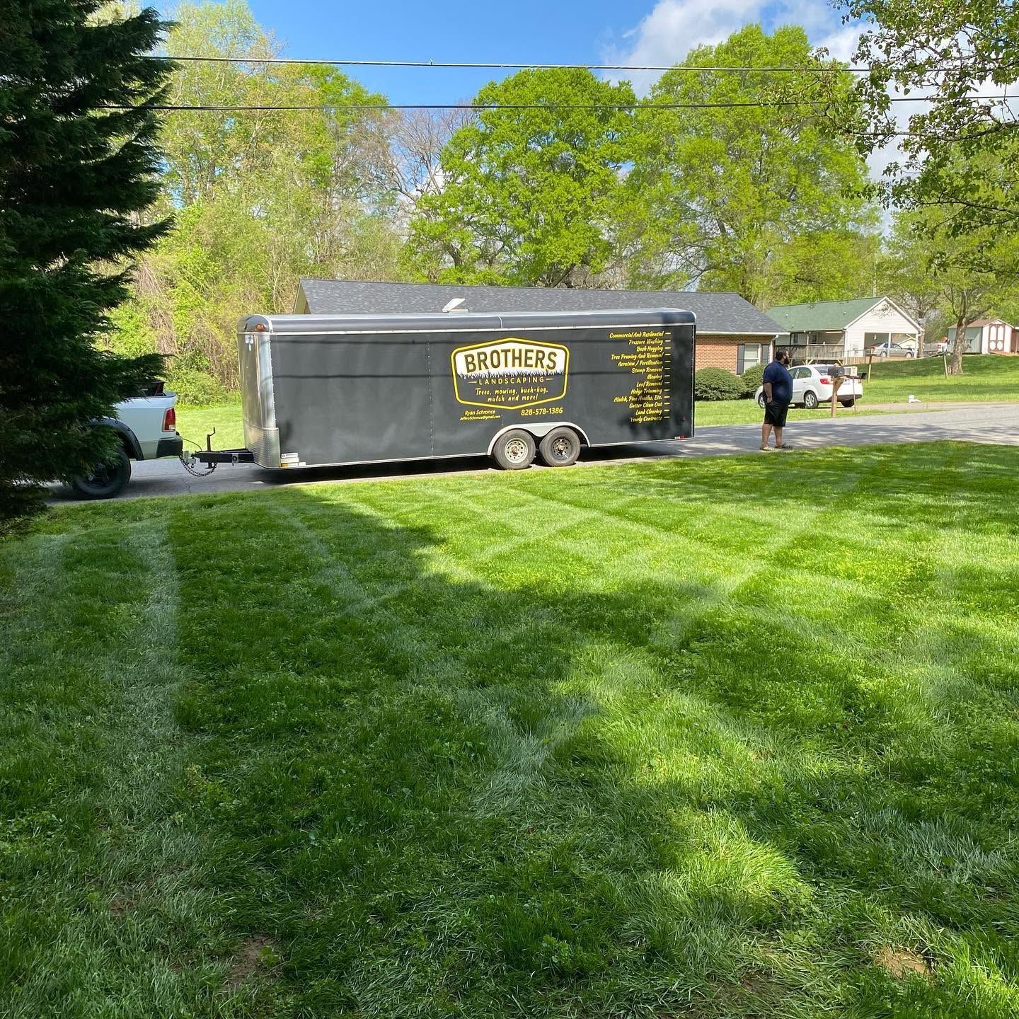 Large black trailer parked on a sunny suburban lawn, with a person standing nearby.