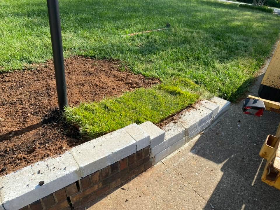 Curb and sidewalk edge with exposed brick retaining wall, grass, and a black pole beside a paved path