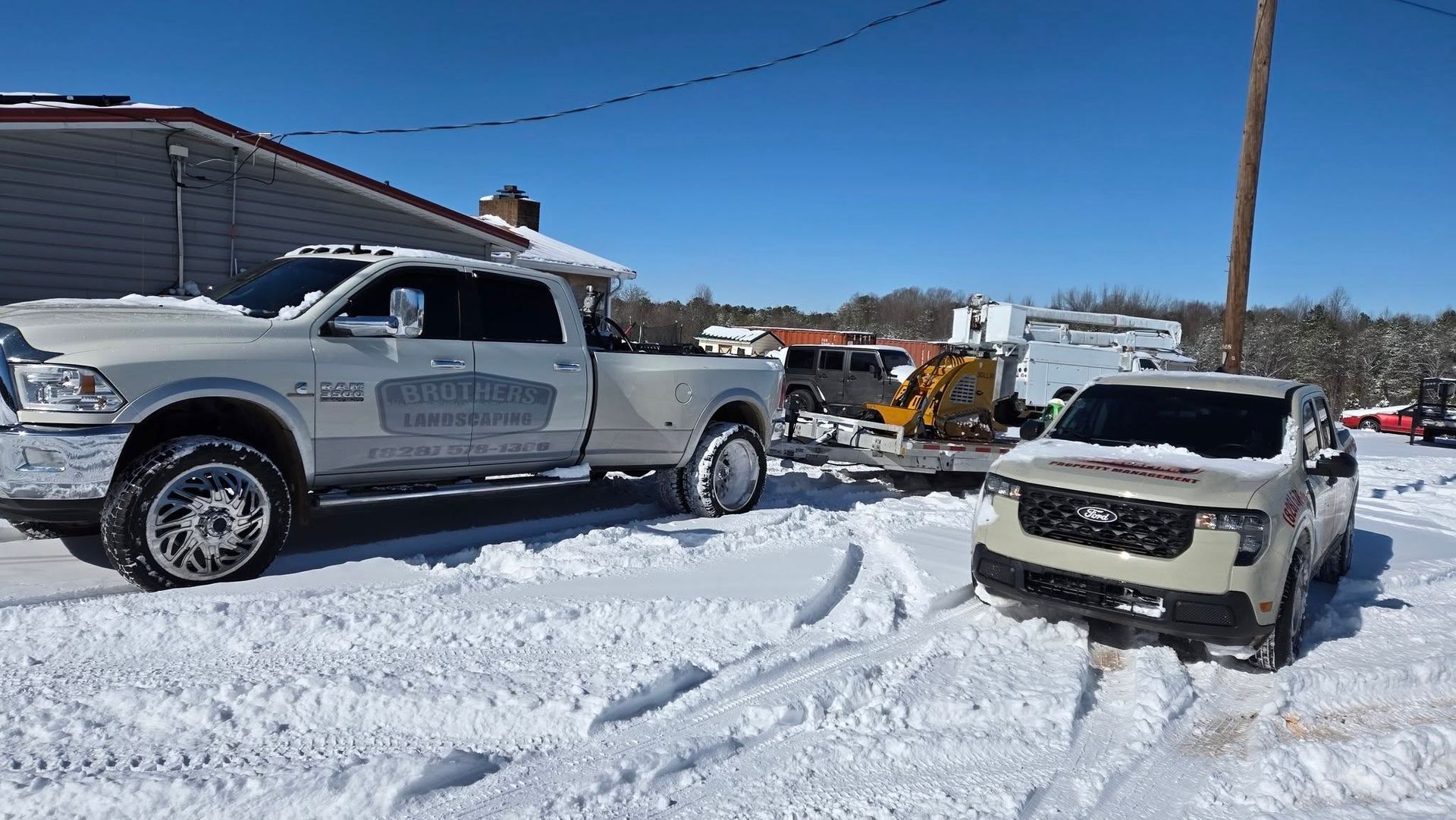Snowy street with a silver pickup truck, white SUV, and a yellow loader in the background.