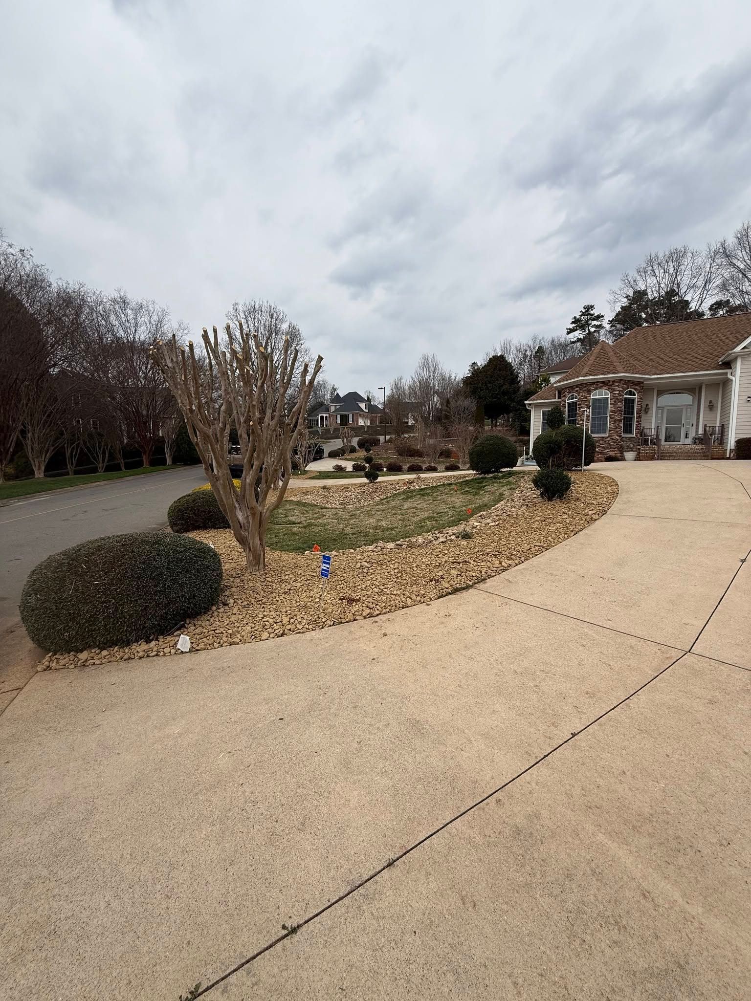 Suburban driveway and front yard with a stone flower bed under a cloudy sky