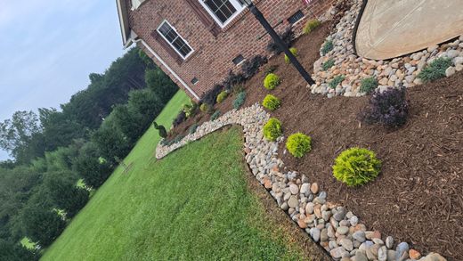 Curved concrete retaining wall with mulch and shrubs along a roadside in a suburban yard