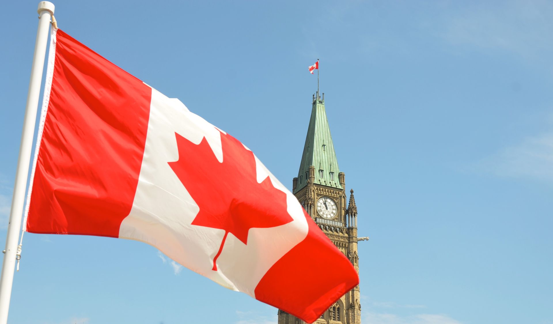 A canadian flag is flying in front of a clock tower