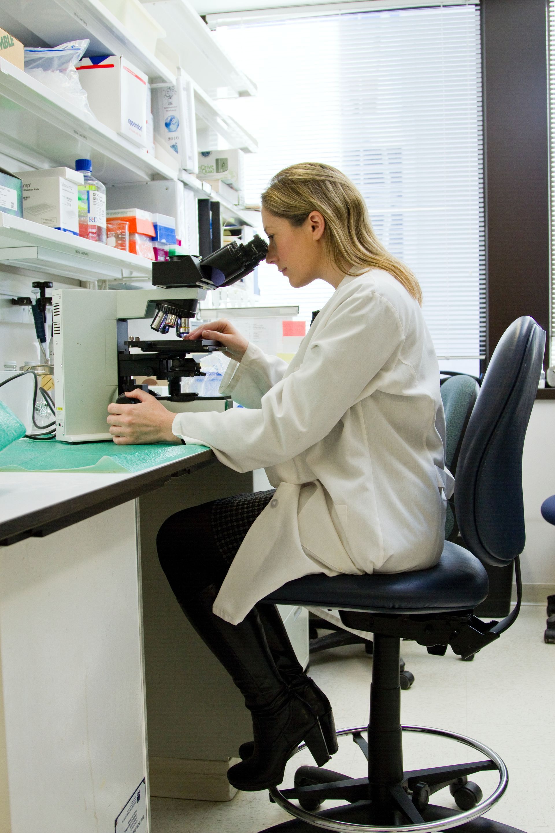 A woman in a lab coat is looking through a microscope.