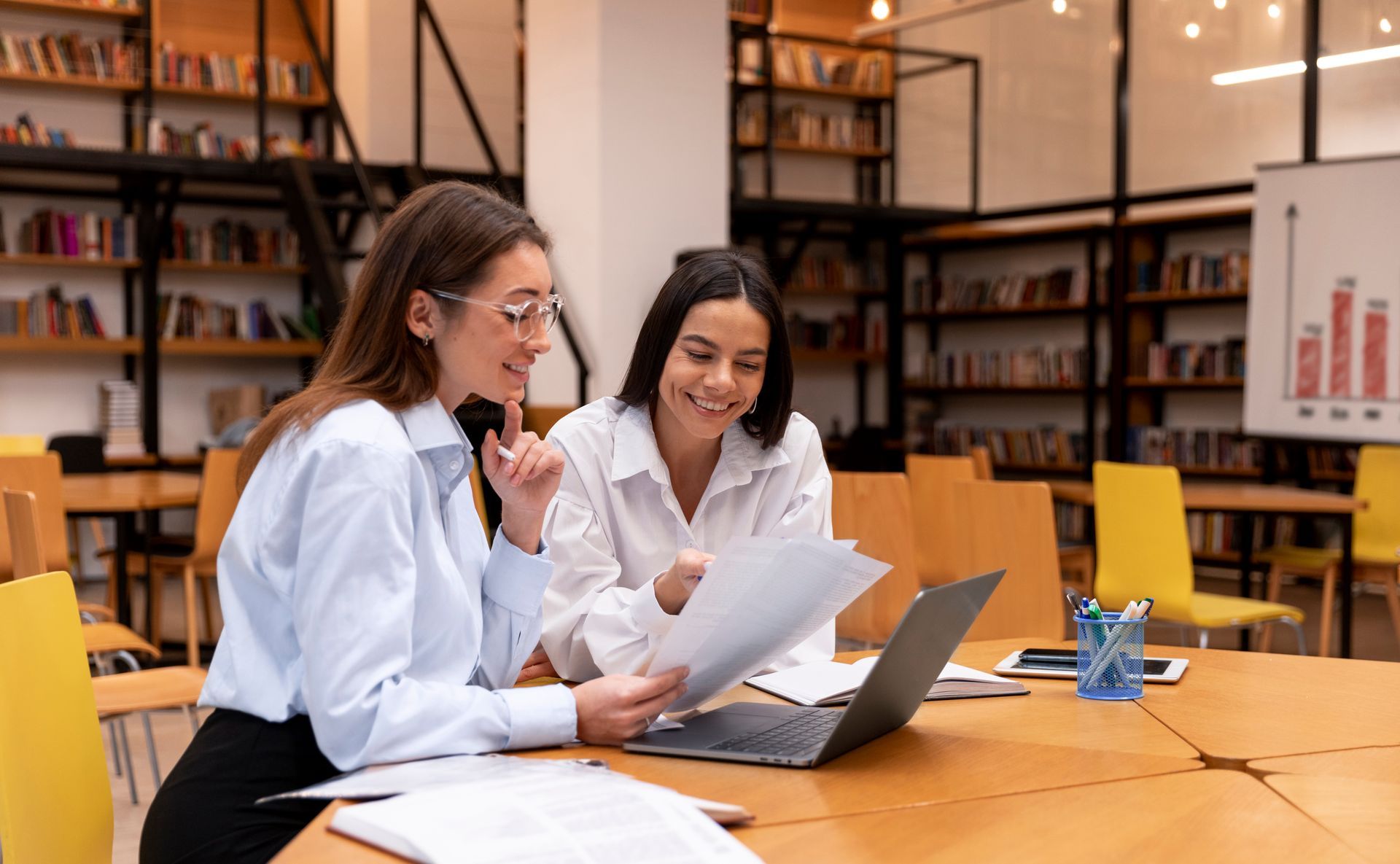 Dos mujeres están sentadas en una mesa mirando una computadora portátil.